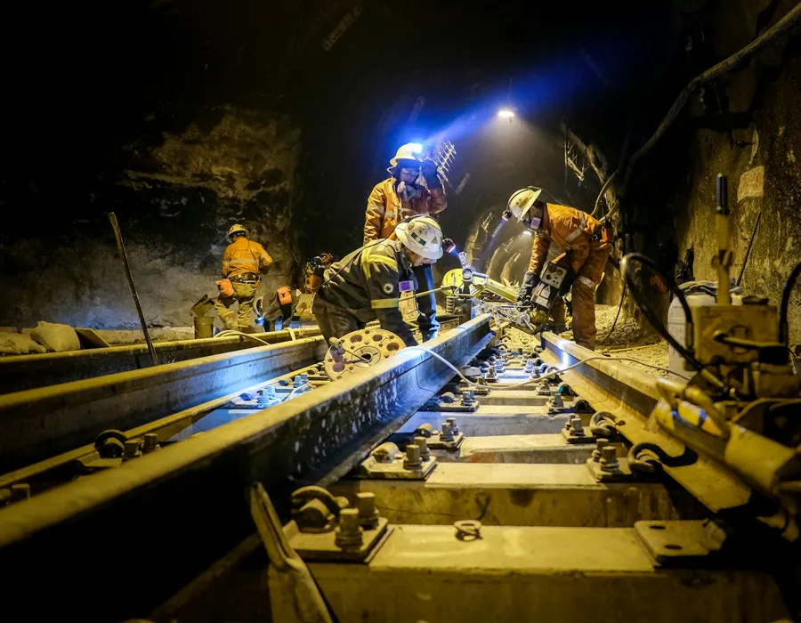 Trabajadores con casco y lámpara realizando mantención de rieles en una mina subterránea